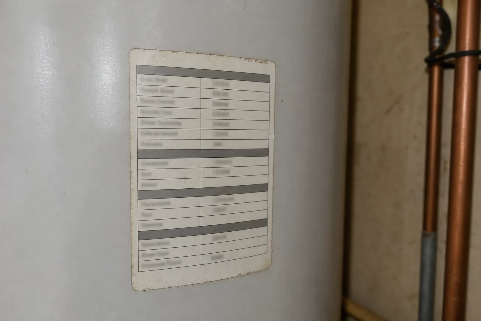 A close photograph of the data plate on the side of a hot water cylinder, the label stating capacity, pressure rating and date of manufacture.